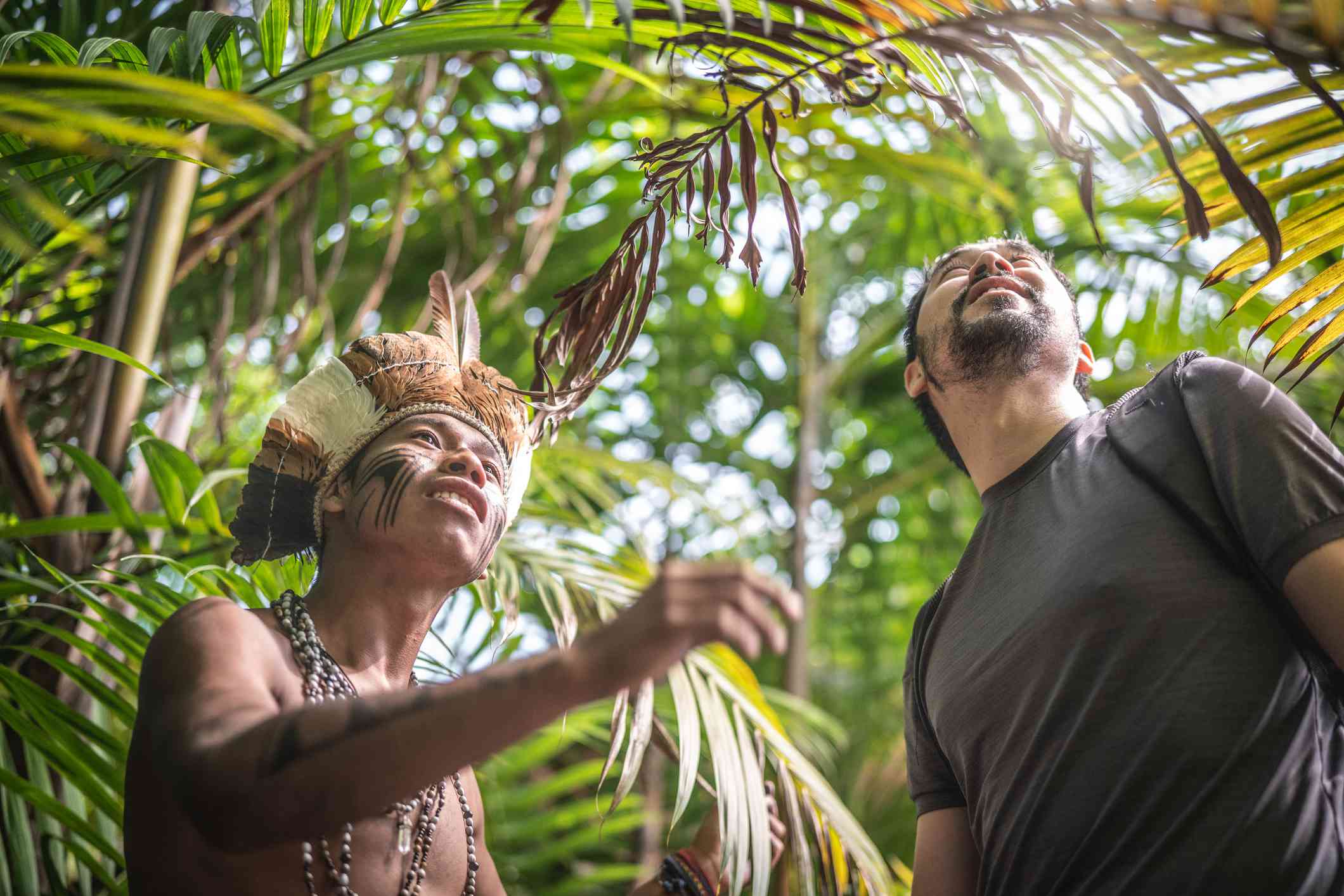 来自瓜拉尼民族的巴西土著青年向游客展示热带雨林＂width=