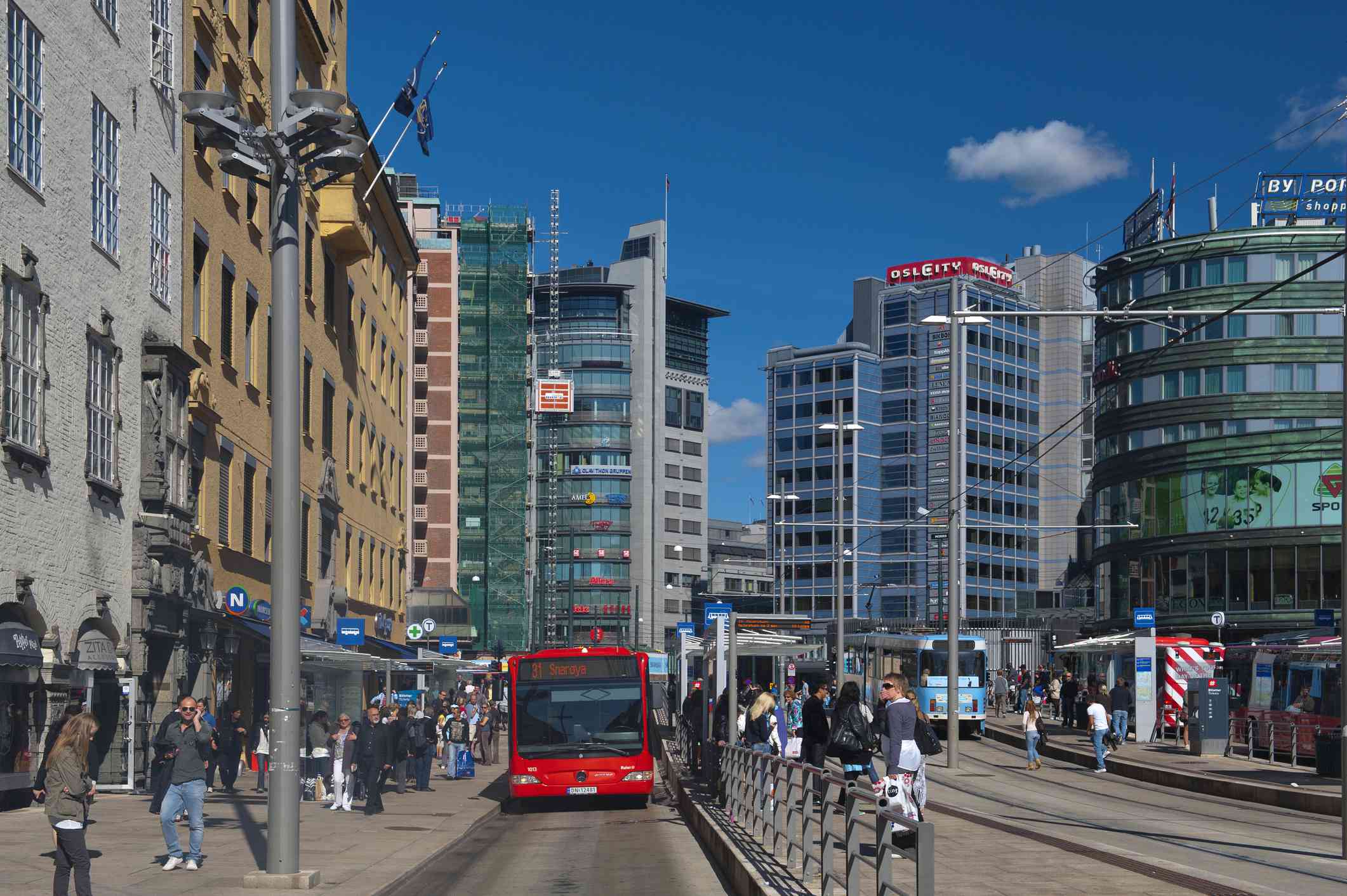 晴空万里、万里无云的晴朗日子里，在挪威首都奥斯陆市中心的高楼大厦上，人们在干净的人行道上行走，中间是一辆红色巴士
