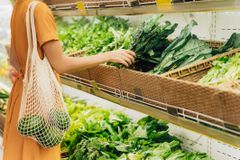 一个女孩在杂货店里拿着一个网眼购物袋，里面装着没有塑料袋的蔬菜。