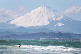 白雪覆盖的富士山远远落后于较小的山脉和冲浪者在蓝绿色的水