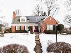 红砖砌成的房子,屋顶和白雪皑皑的草坪上太阳能电池板前景。