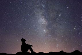 一个人坐在地上仰望星空的剪影