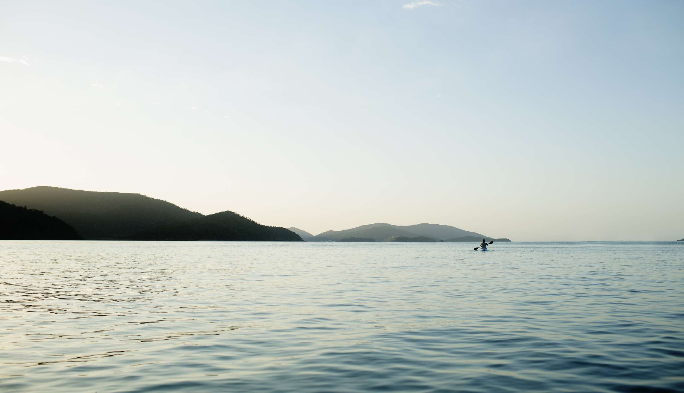 孤独的皮划艇者在昆士兰海岸的圣灵群岛的蓝色水域中，清澈的蓝天和远处的山丘