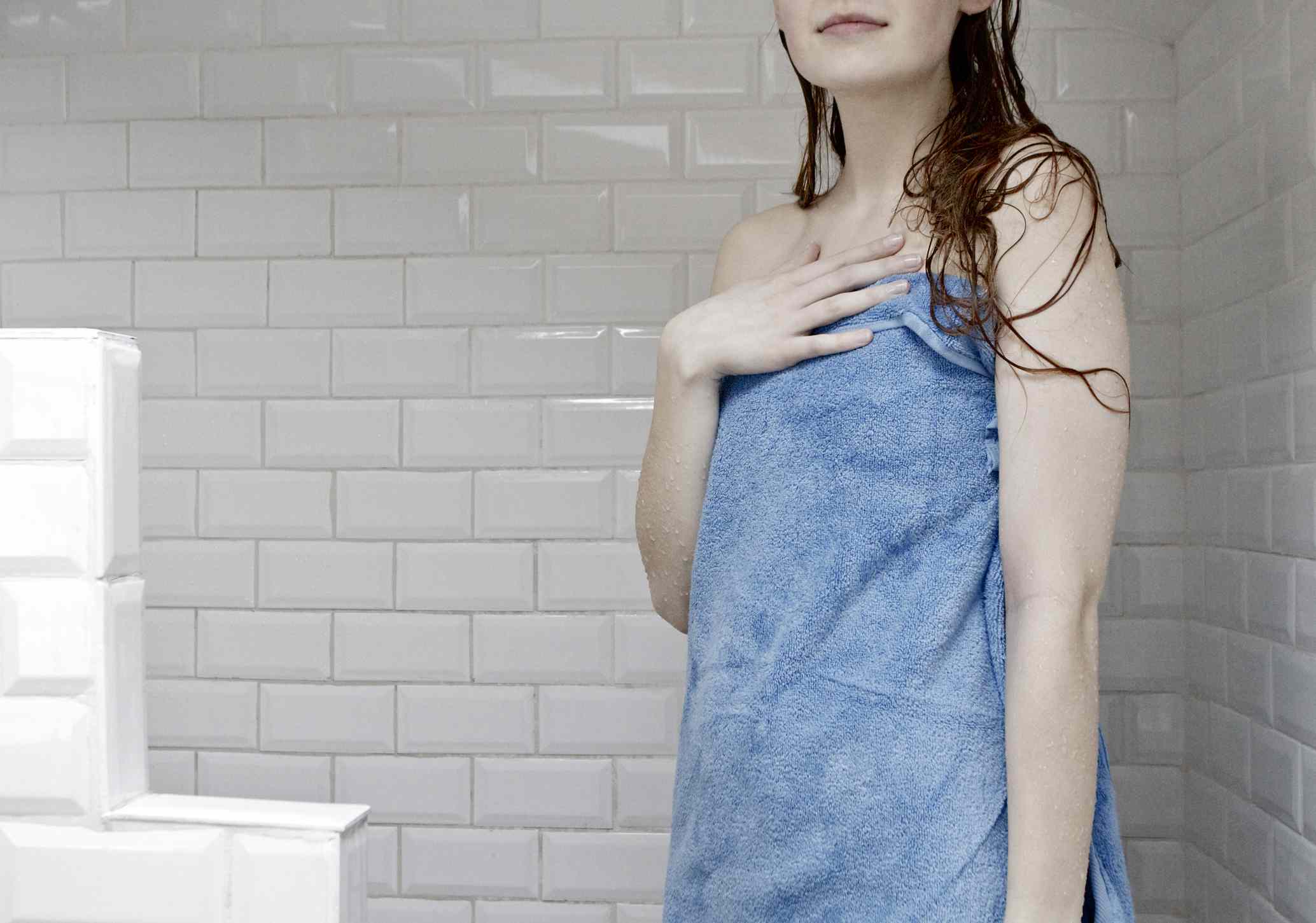 一个裹着蓝色毛巾的湿女人在白色的地铁瓷砖淋浴间里。