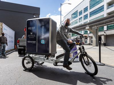 一名男子戴着口罩骑在城市货运实验室的电子货运自行车上。
