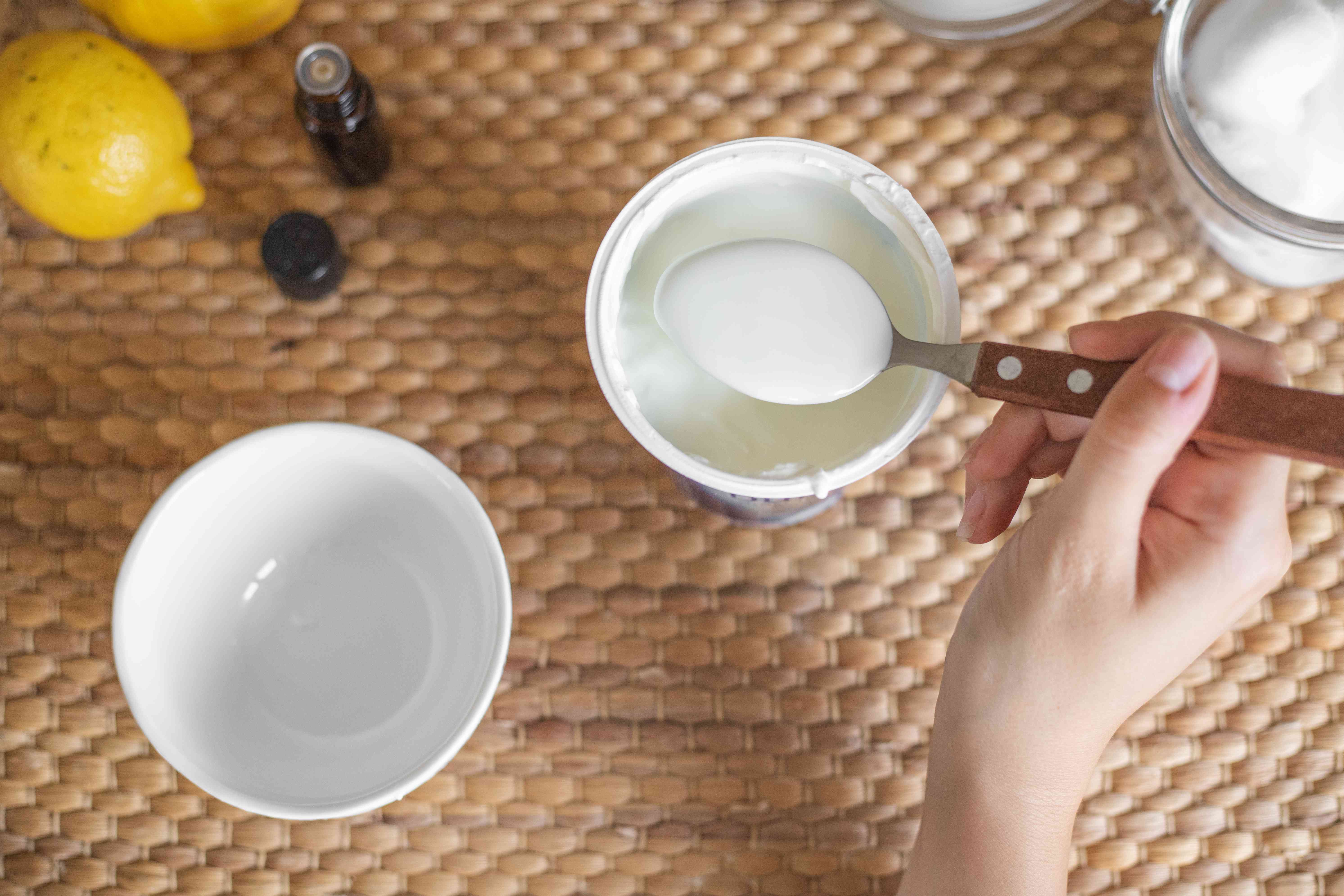 用手量出几汤匙酸奶，从杯子里倒入白色的陶瓷碗里