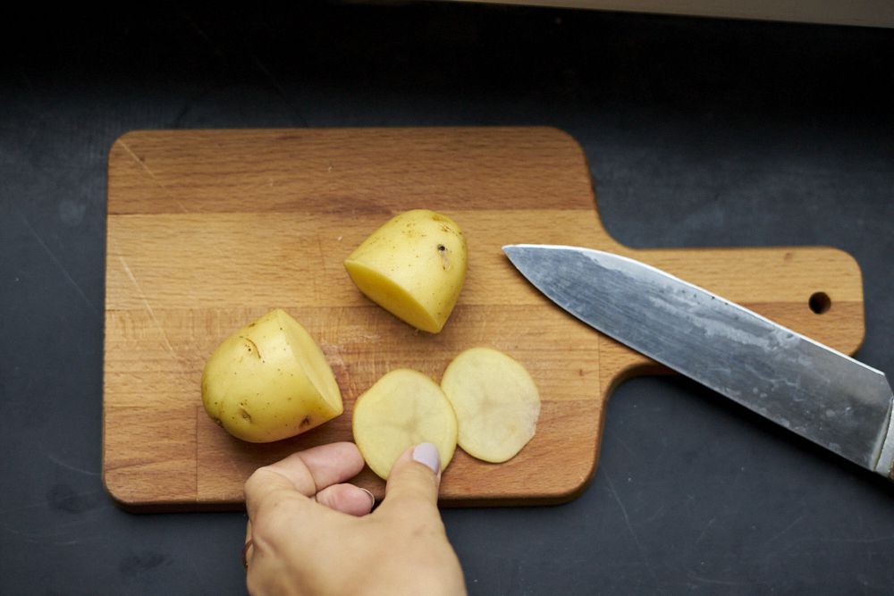 剥皮的土豆在切菜板上被切成薄片，用刀将黑眼圈切成薄片“width=