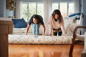 两个女人在客厅里铺一个地毯“width=