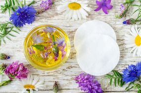 小玻璃碗芳香化妆品油与鲜花提取物和化妆棉。天然护肤和自制化妆品概念。