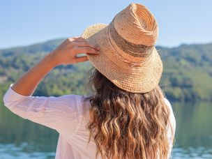 一个戴着大草帽的女人在炎热的夏天站在湖边