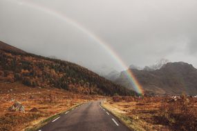 彩虹在道路上，背景有山“width=