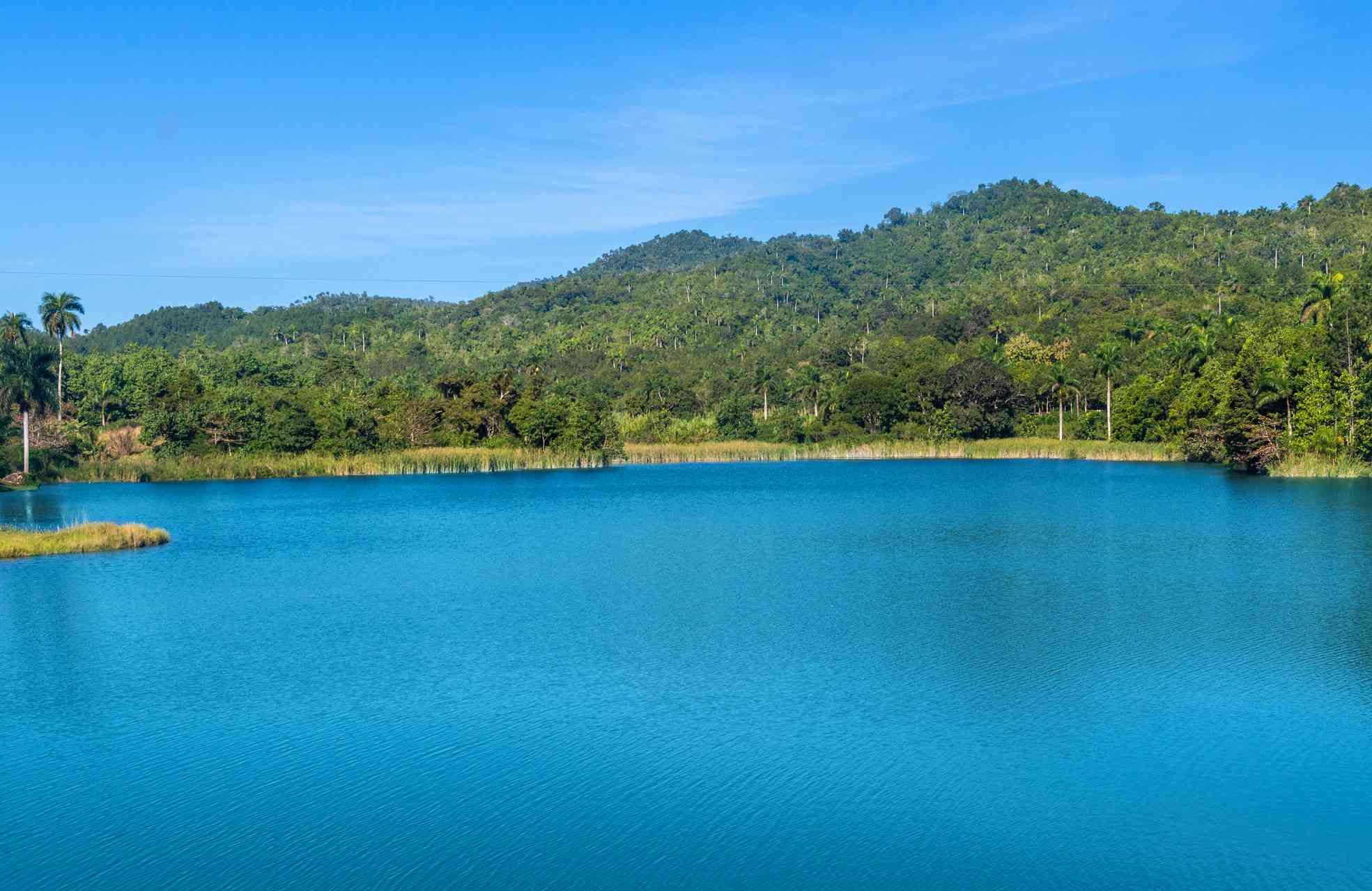 茂盛的森林和山脉围拢的宽敞绿松石蓝色湖，在蓝天下覆盖着在拉斯特拉扎斯