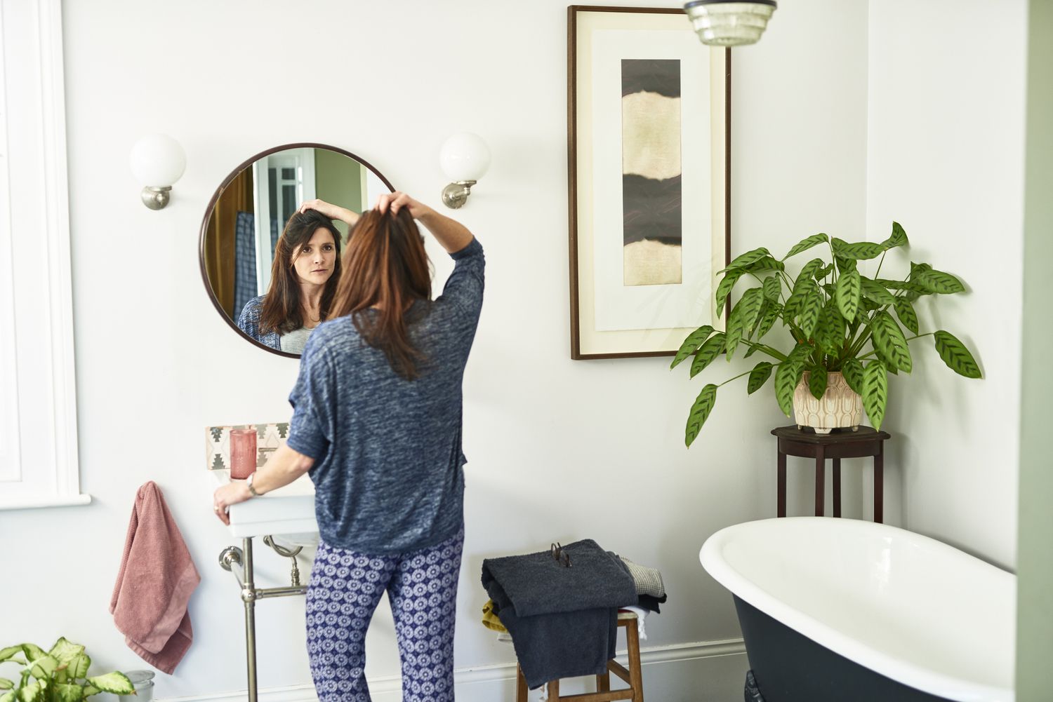 一个白人妇女在明亮的白色浴室里照镜子，摸着自己的头发。