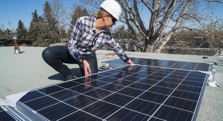 一名建筑工人正在住宅屋顶安装太阳能电池板。＂class=