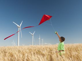 一个小男孩在有风力涡轮机的田野里放风筝。”width=