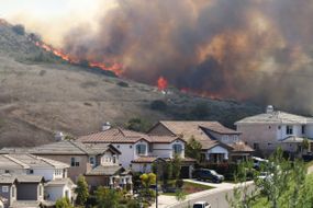 Wildfire burns near a neighborhood on a sunny day