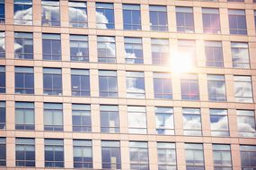 阳光从许多窗户上散发出建筑物；窗户用一些云层反映阳光明媚的天空。“width=
