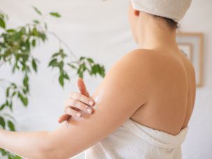 女人淋浴后用白毛巾裹着，涂乳液保湿剂