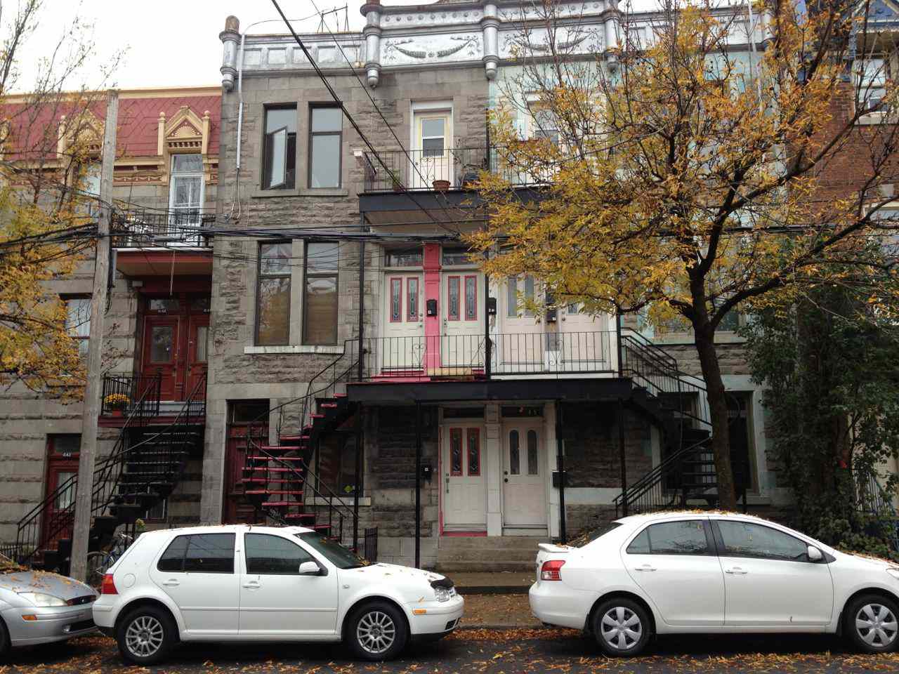 蒙特利尔城市房屋的图片，前面有两辆白色汽车。