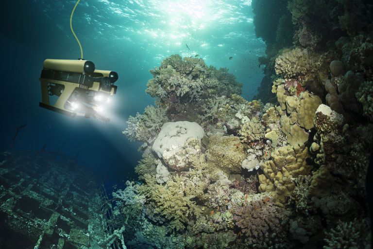 一个机器人带着前灯探索水下暗礁。一根绳子挂在机器人上。＂class=