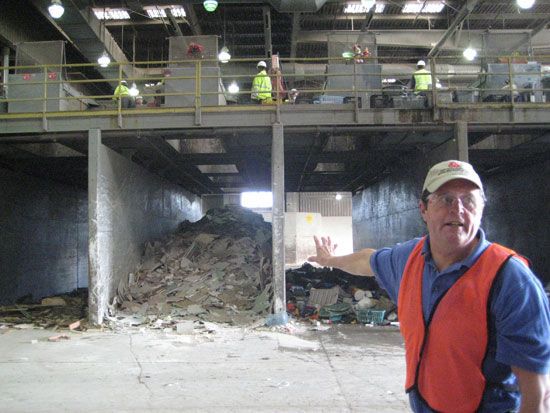 一名穿着防护装备的男子指着废物处理设施中的垃圾做手势。