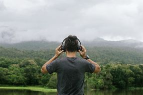 男人一边听音乐一边看湖边的山的后景＂width=