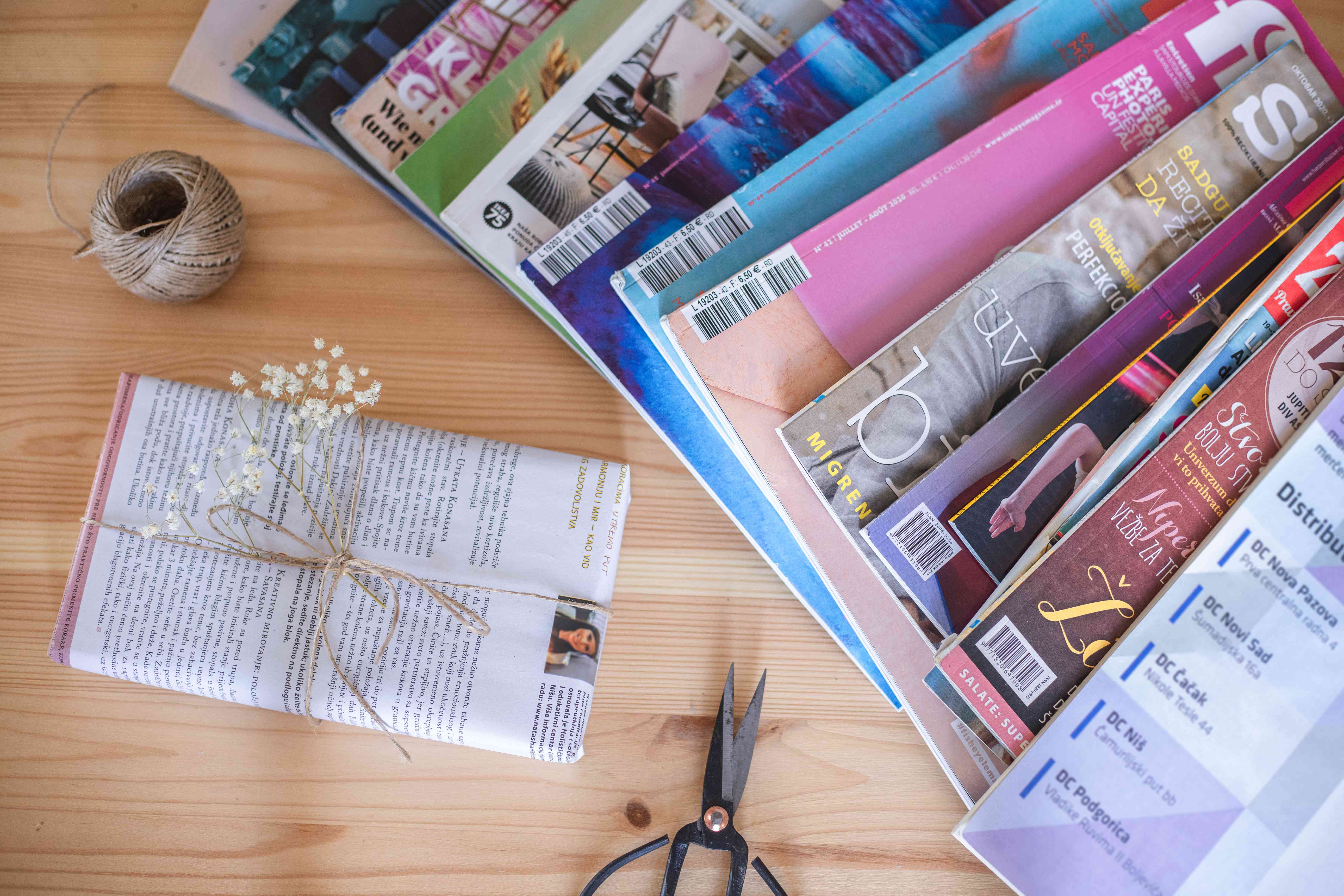 在剪刀，麻线和礼品包装的桌子上散布在桌子上的杂志中“width=