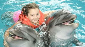 生活夹克中的小女孩在一场海豚遭遇期间拥抱两只海豚“width=
