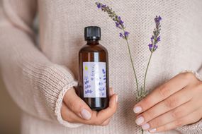 woman in sweater holds DIY lavender oil and a sprig of dried lavender flower