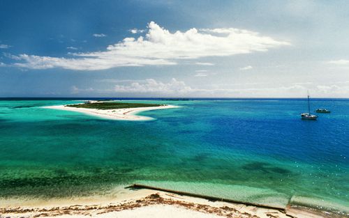 在Dry Tortugas的一个小岛上，两艘船就在近海，鸟瞰明亮的白色沙滩，周围是浅蓝色和蓝绿色的水域