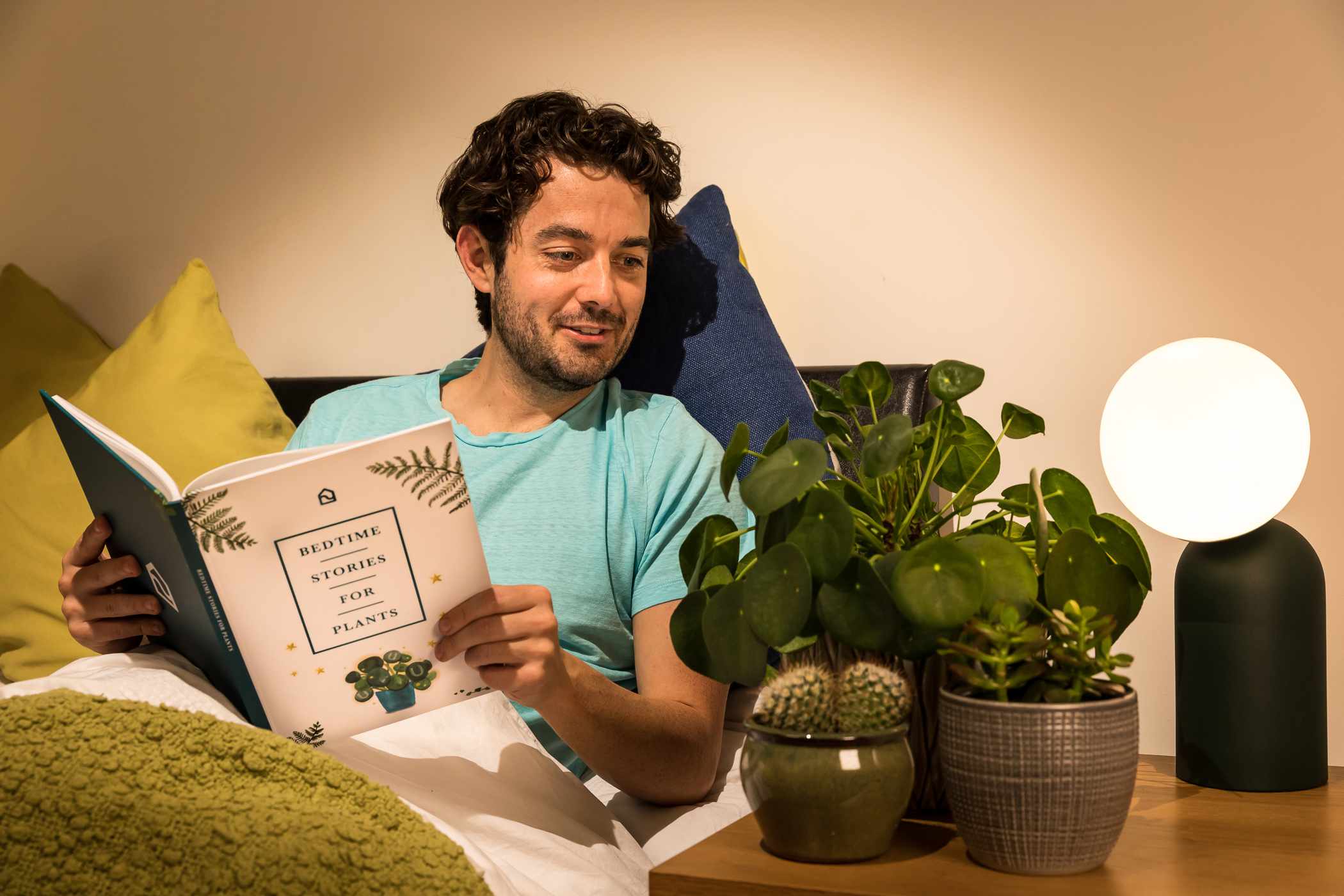 一个躺在床上的男人对着他的三株植物读书