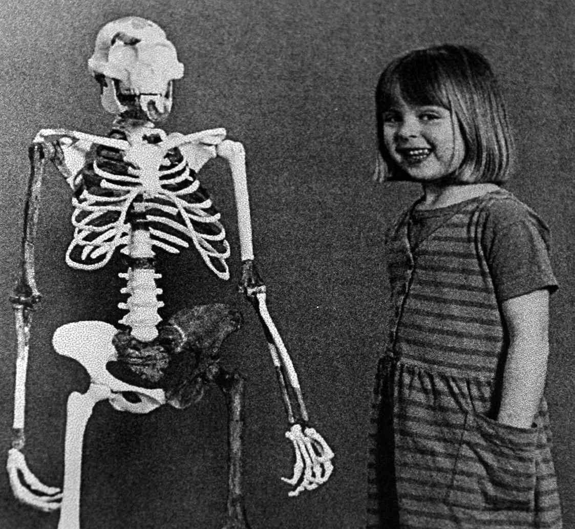一个人类小孩在成年南方古猿阿法种的骨架旁摆姿势