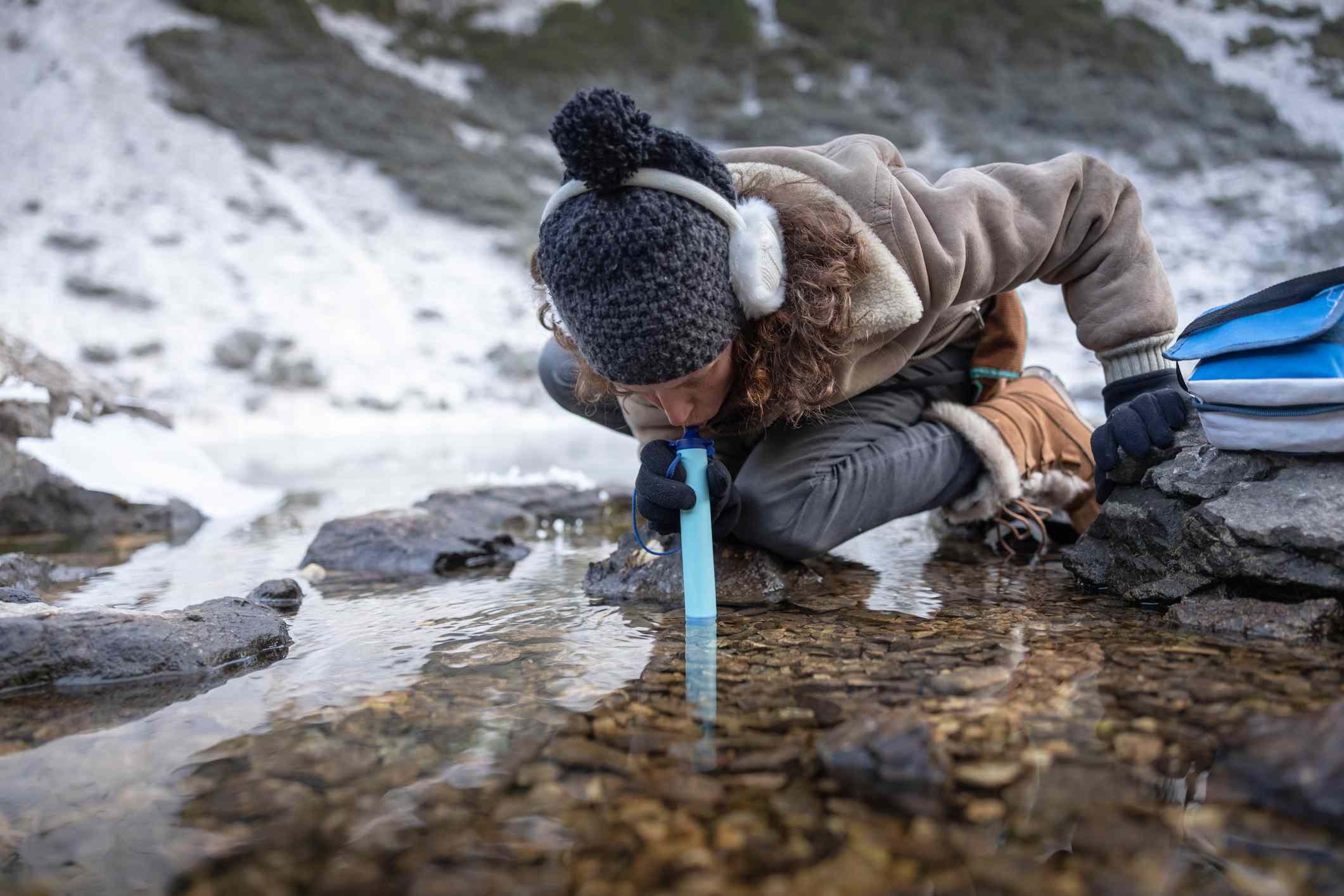 女人在溪流中使用水过滤稻草在冬天“width=
