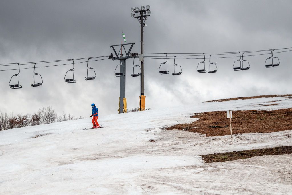 过去一个人滑雪板空椅子电梯和一片草在滑雪胜地,不得不关闭一些斜坡由于缺少雪,