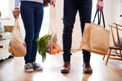 关闭回到家的夫妇从购物旅行运载在塑料自由袋子的杂货