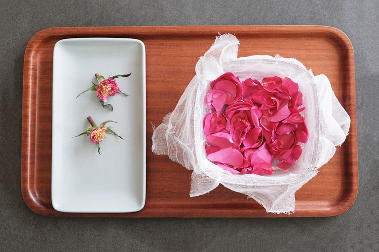 新鲜采摘的粉红玫瑰花瓣在奶酪布衬里的碗旁边的白色托盘与空花蕾