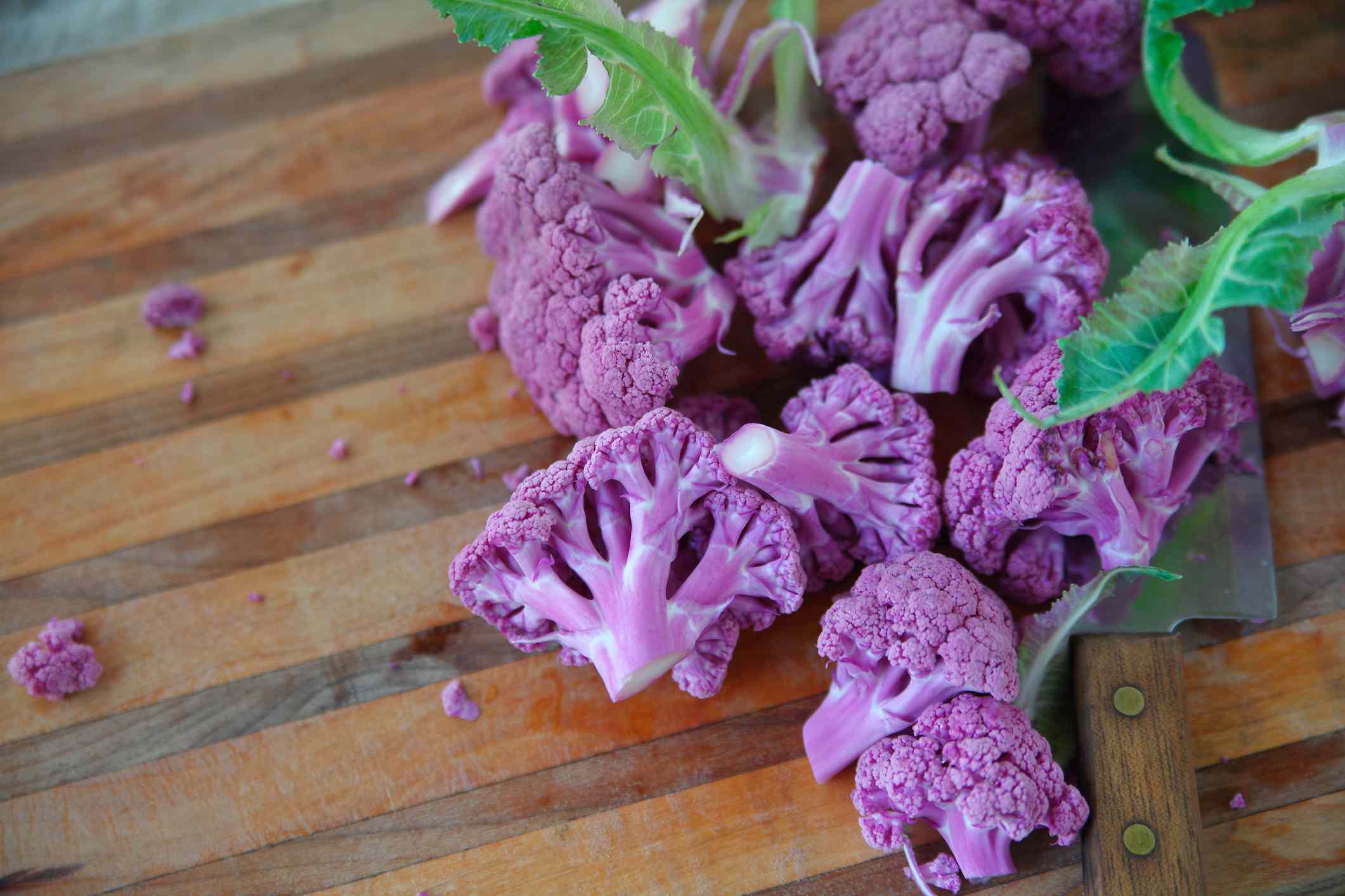 紫色烤花椰菜配绿叶放在木砧板上