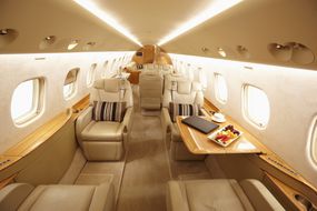 一架昂贵的私人飞机内部，有真皮座椅和水果托盘＂width=