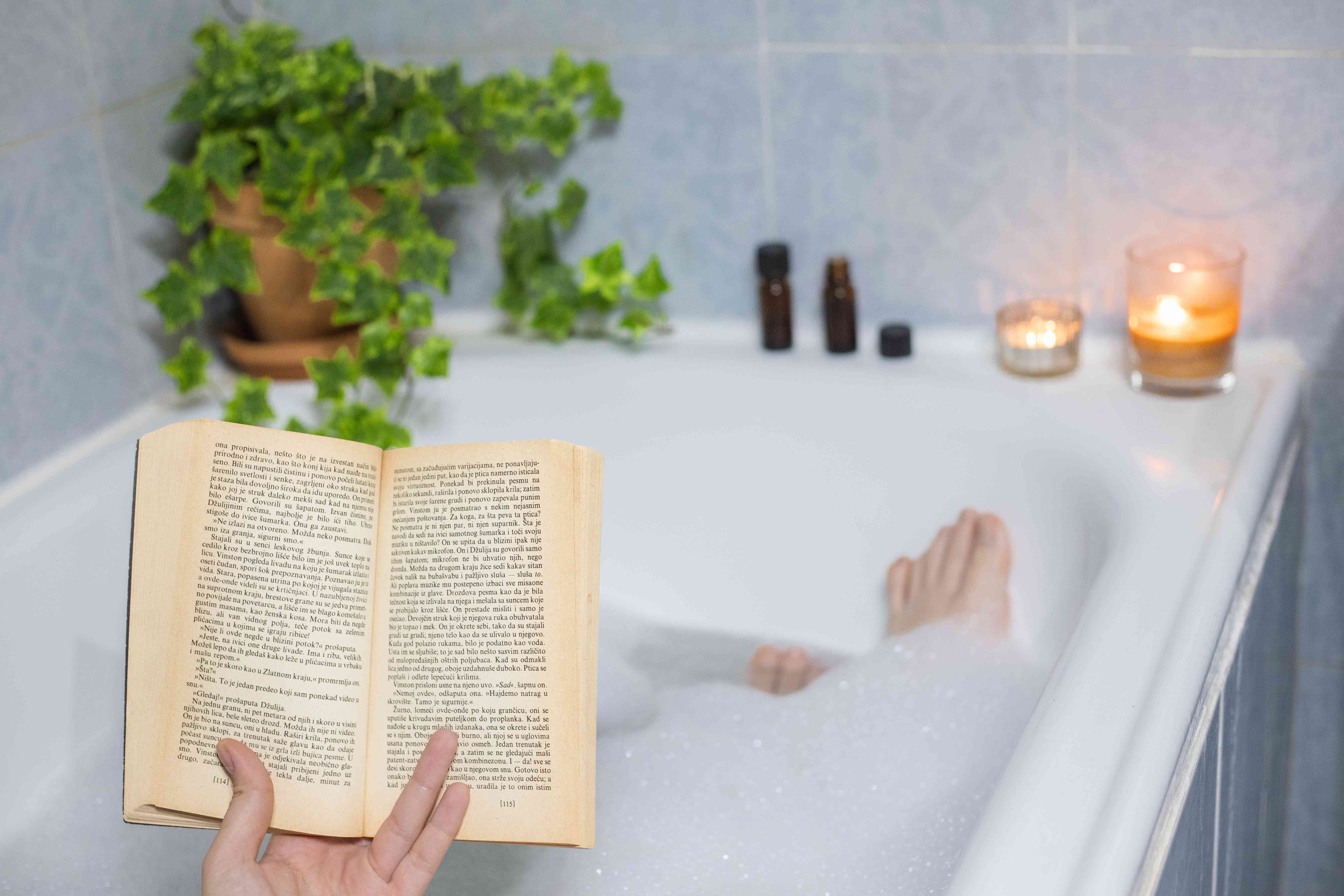 人在读书的时候,泡泡浴放松蜡烛点燃和常春藤植物”width=