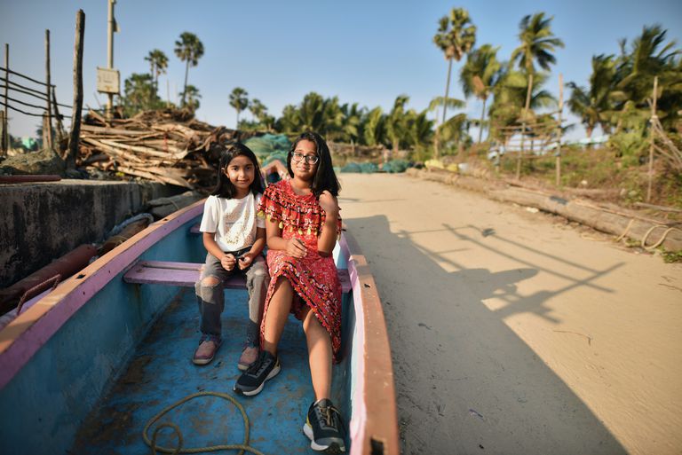 两个年轻女孩坐在印度乡村海岸线上的一艘渔船上＂class=