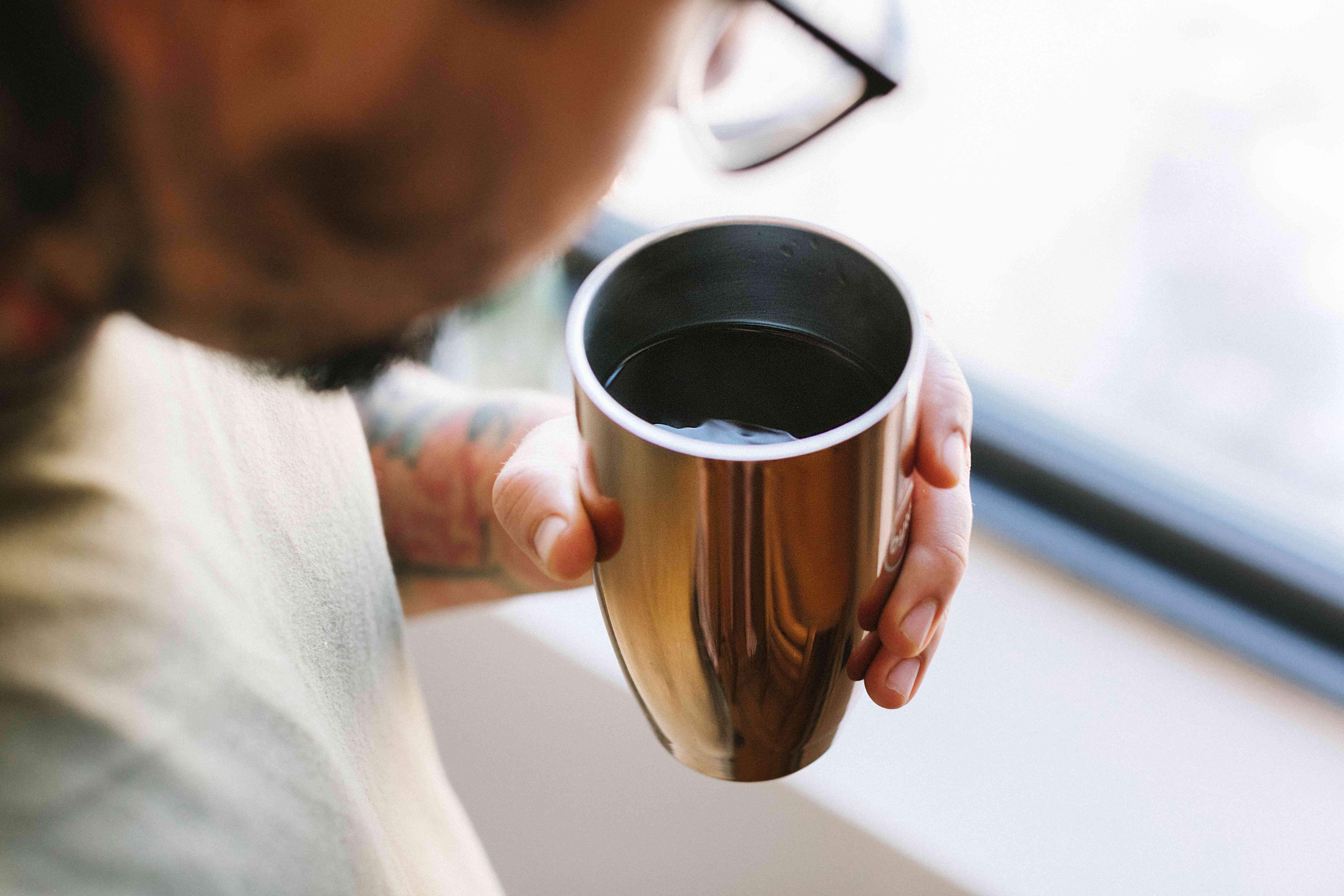 在可重复使用的杯子里喝一杯热咖啡的眼镜的人