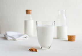 玻璃杯和瓶子的牛奶和生杏仁放在桌子上＂width=