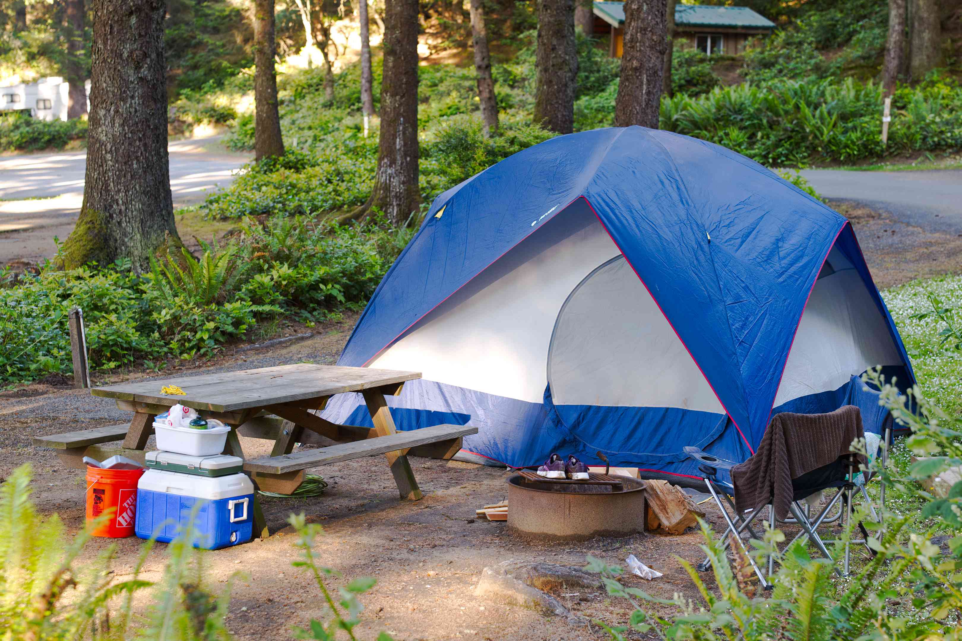 蓝色和白色的帐篷营地野餐桌上包围,冷却器和野营装备
