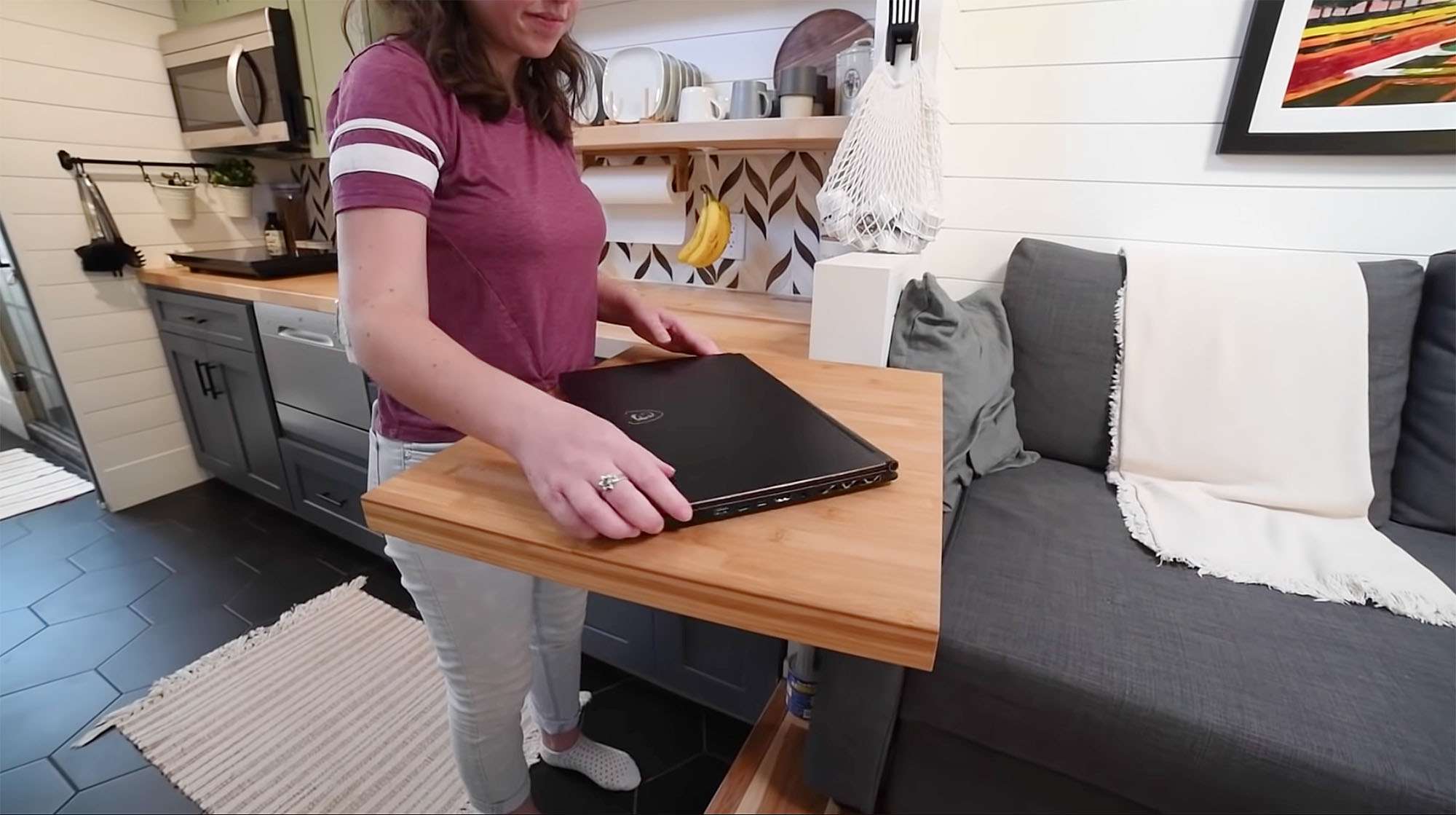 Sydne Gold设计的一所小房子的内部，在厨房和沙发附近的一张可拉出的桌子上，小金拿着一台笔记本电脑。