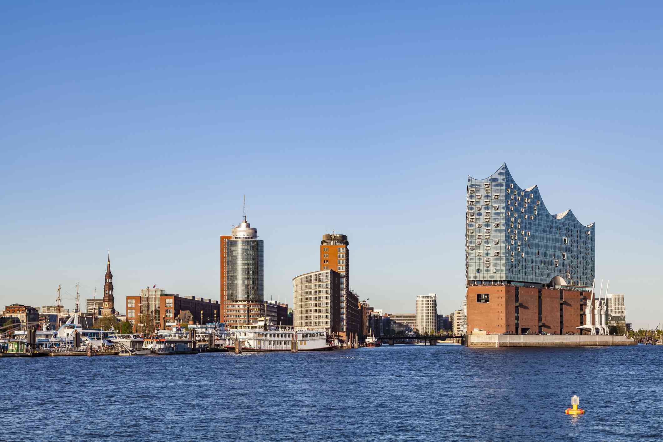 从右边的汉堡爱乐港(elbphilharmonie Hamburg)的蓝色水域望过去，这是一座2017年完工的多功能建筑，底层有几层砖，上面有一座现代的玻璃塔，紧挨着汉堡港口的新老建筑，