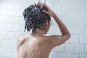 一位亚洲妇女在一间铺着白色瓷砖的浴室里用水洗头。