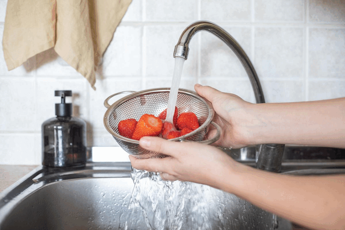 手在水槽中的金属漏勺中洗净新鲜的草莓