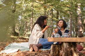 一个女人和男人享受喝茶坐在树林里一条毯子。他们都穿着毛衣。