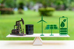 化石燃料vs可再生/未来的清洁替代能源概念:石油抽油机，原油桶桶，太阳能电池板，绿叶电池，风力涡轮机在木材平衡秤在平等的位置。＂width=