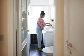 打开的门显示一个穿着工作服的孕妇在浴室的水槽里洗手
